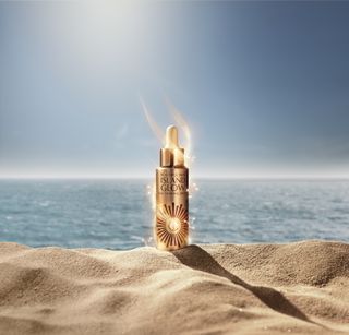 A bottle of Charlotte Tilbury Island Glow on a beach.