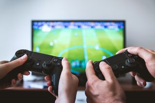 Two people holding black xbox contro9llers in front of a tv screen with a soccer field on it