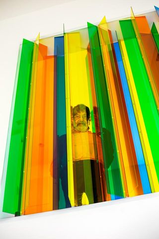 Carlos Cruz-Diez standing behind coloured glass panels