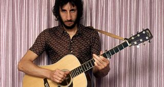 A portrait of a long-haired Pete Townshend playing a Martin dreadnought capoed at the 5th fret, with striped curtains in the background.