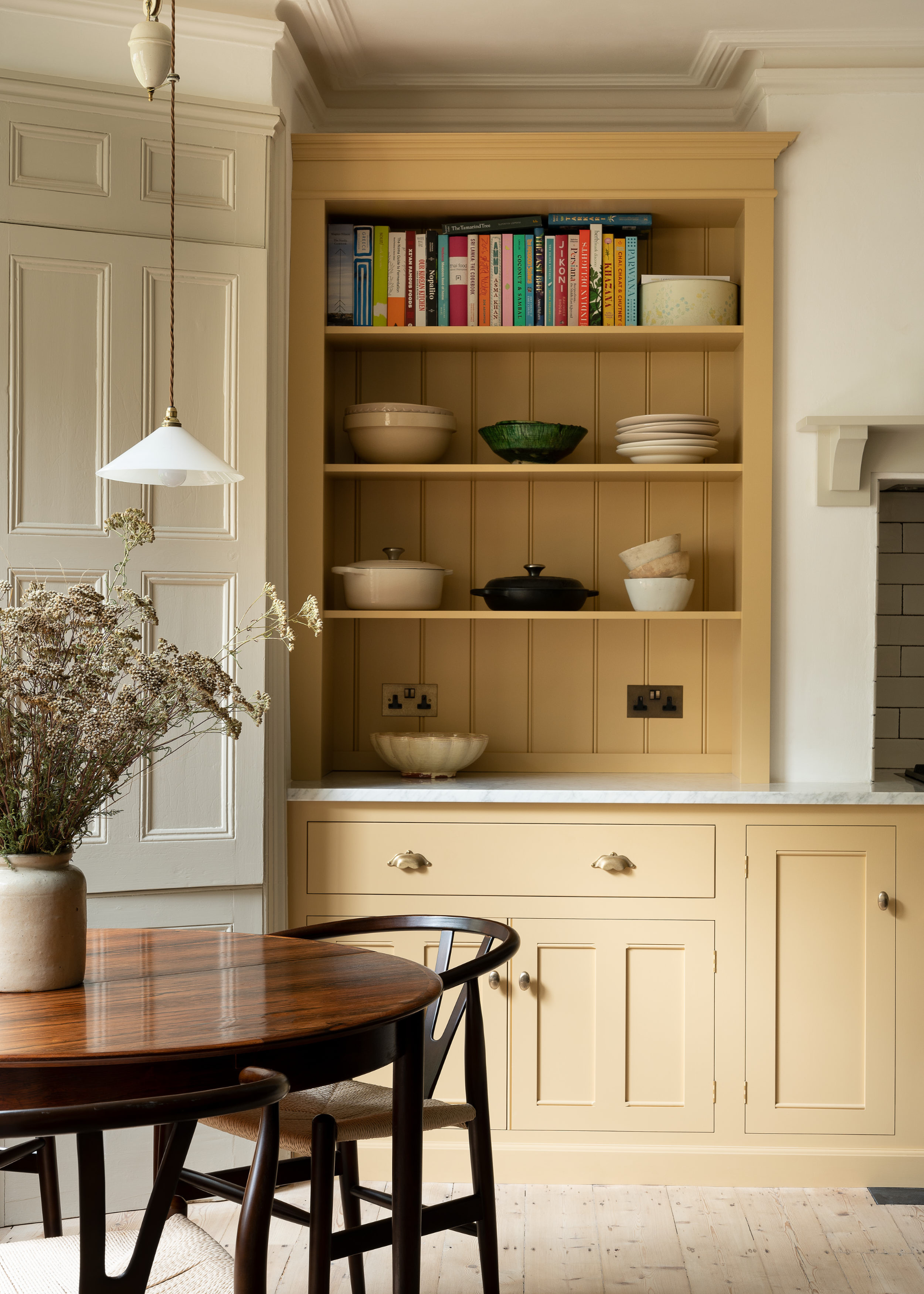butter yellow kitchen with open shelving and a dining table in the kitchen with a large planter and stems inside