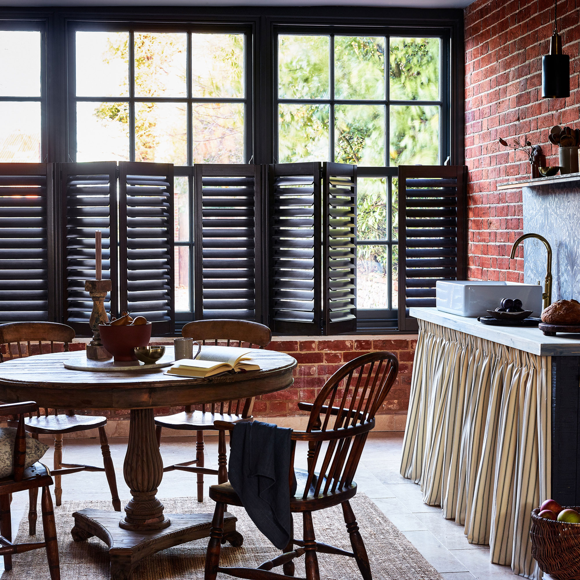 kitchen with exposed brick walls and round dining table and black window shutters