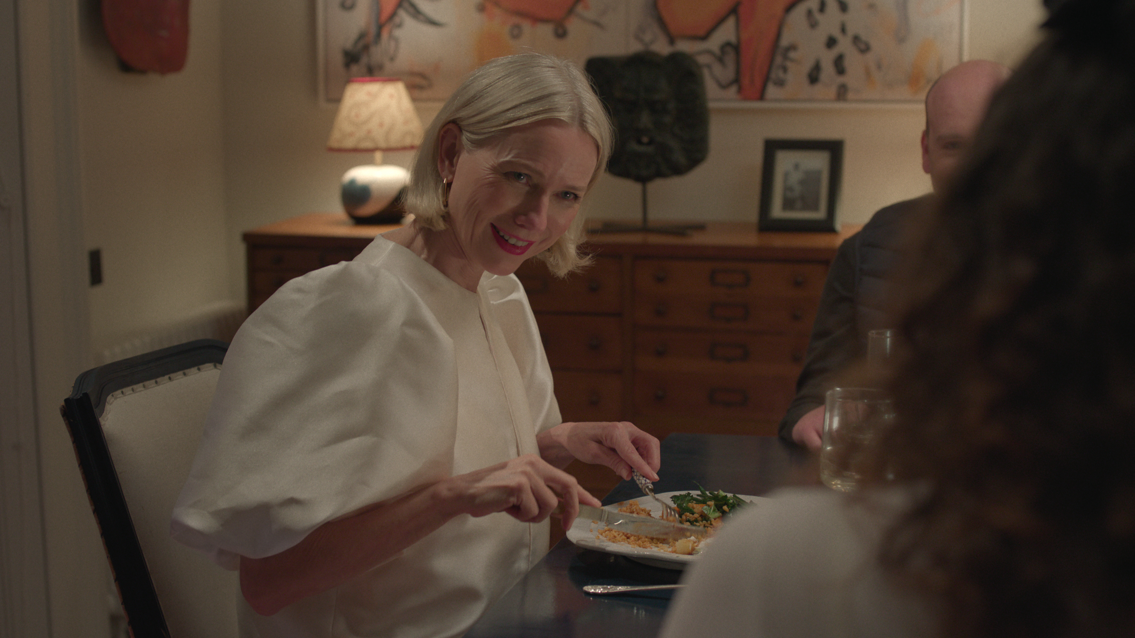 Ann in a white top eating dinner in Too Much