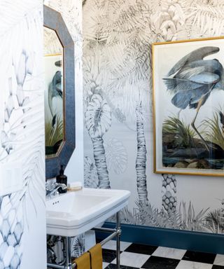 Small bathroom with checkered floor, large painting with crane, blue mirror, blue linear palm tree wallpaper, blue skirtings
