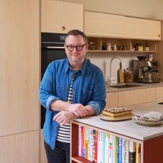 Man standing next to a cake in front of the plywood kitchen