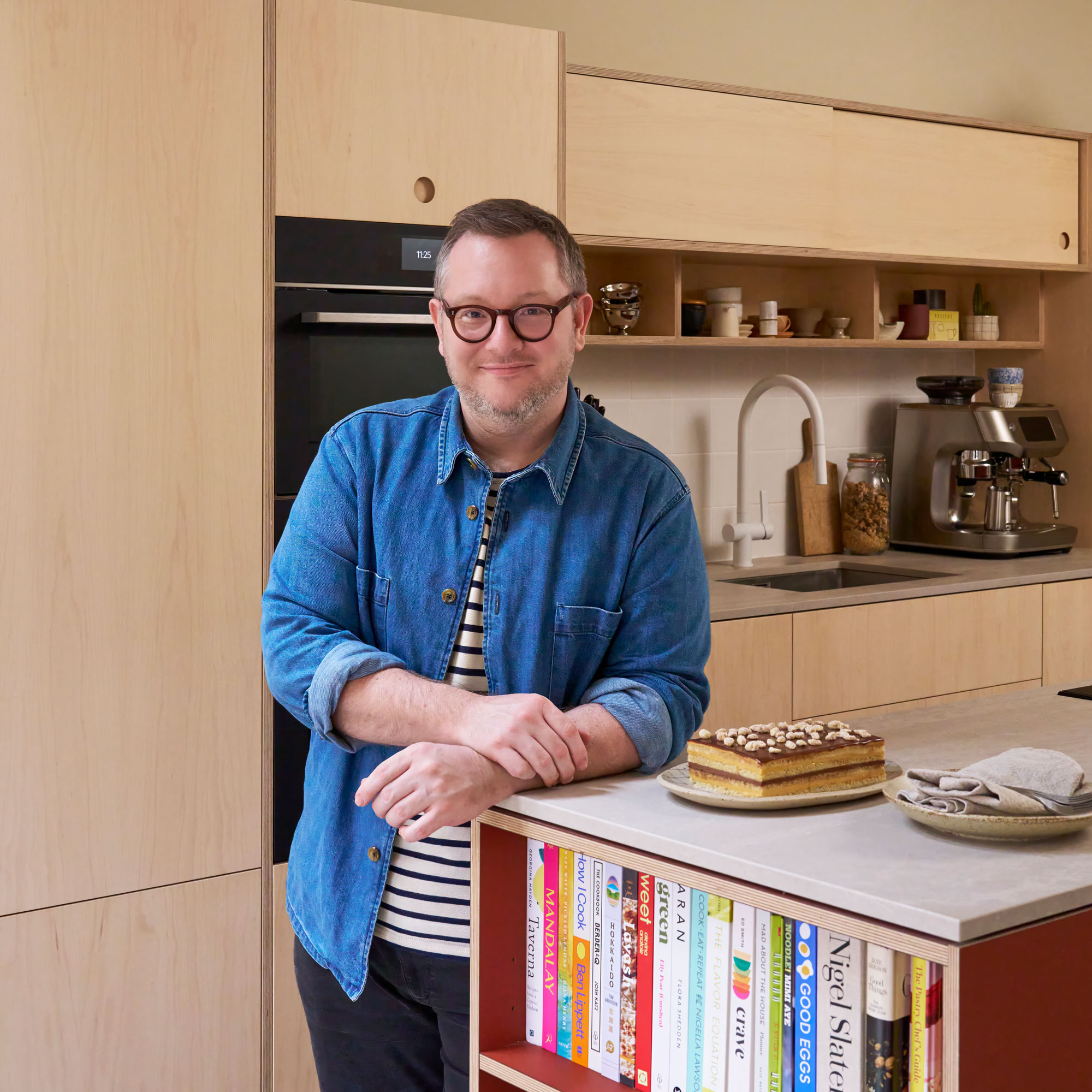 Man standing next to a cake in front of the plywood kitchen