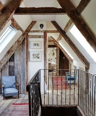 exposed beams in a landing of an old farmhouse decorated with rugs and chairs