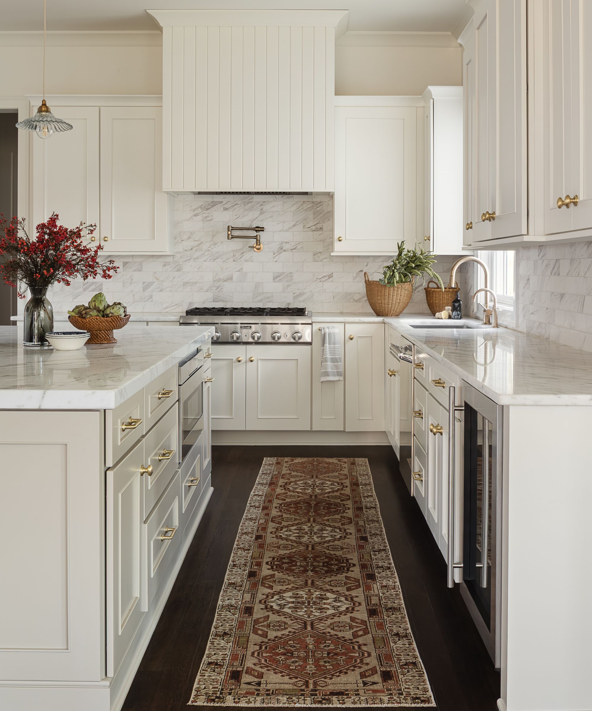 a white traditional kitchen with an enclosed paneled kitchen hood with a coordinating kitchen island with marble countertops and a vintage rug
