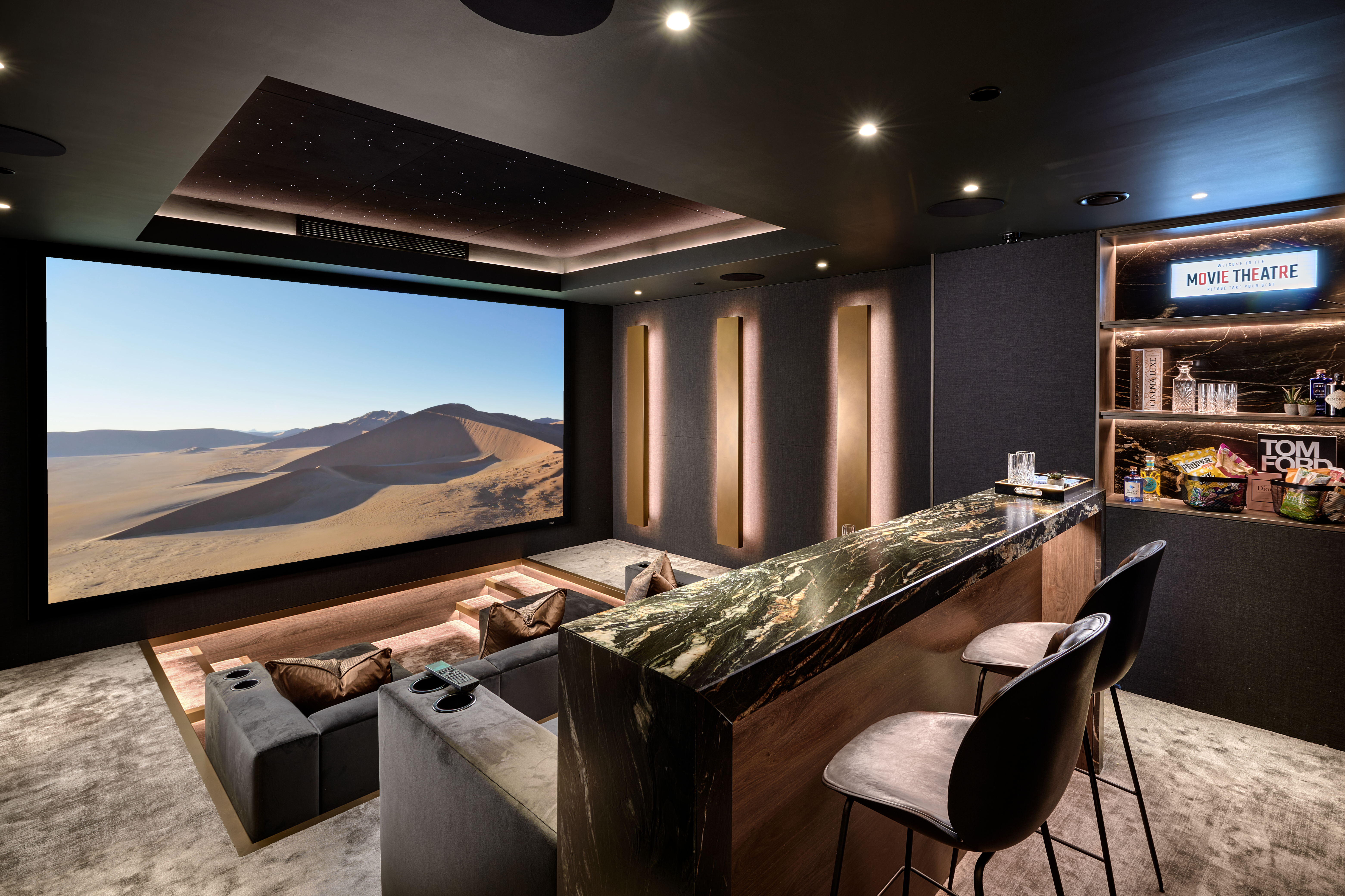 A home theater room showing sofas, a projection screen and warm bronze lighting