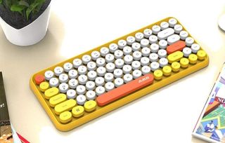 Ett Felicon-tangentbord i gult, orange och vitt som ligger på ett vitt skrivbord bland lite böcker.