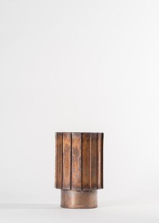 Handcrafted vessel made from metal with vertical rectangular panels going around the sides.