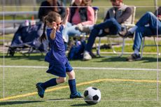Little girl playing football as parents watch from the sidelines