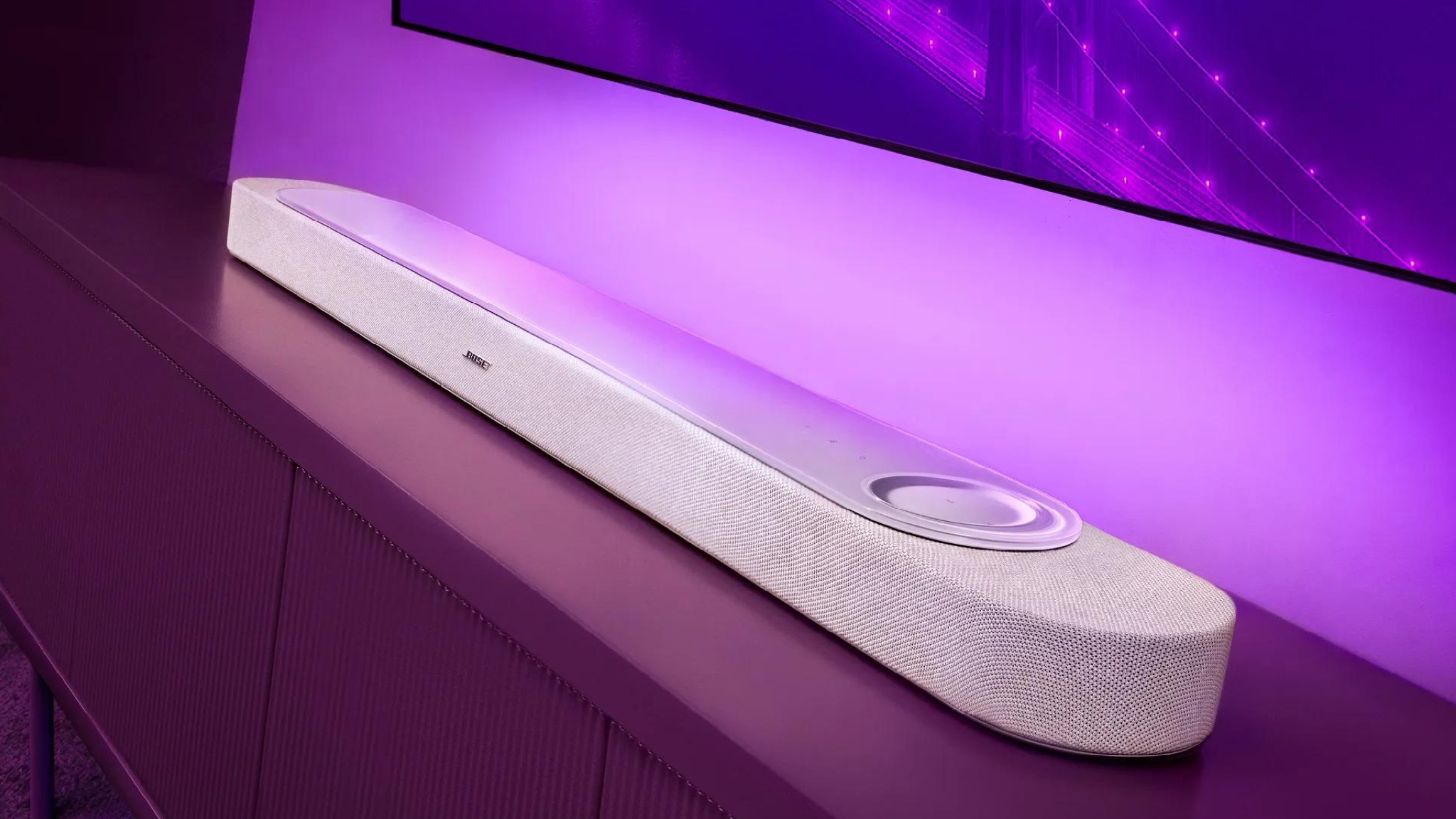 Bose Lifestyle Ultra soundbar in white below a TV with purple ambient lighting