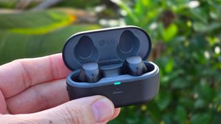 LG Tone Free T90S earbuds in charging case held up in front of a garden.