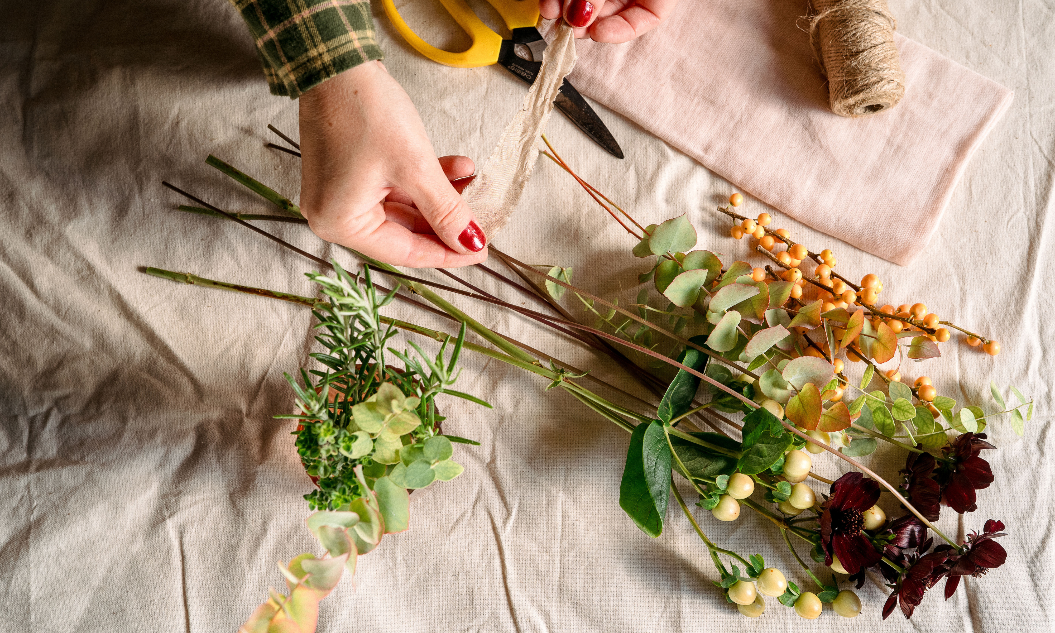 Aerial shot of a table with flowers, twine, scissors, pink napkin and berries on