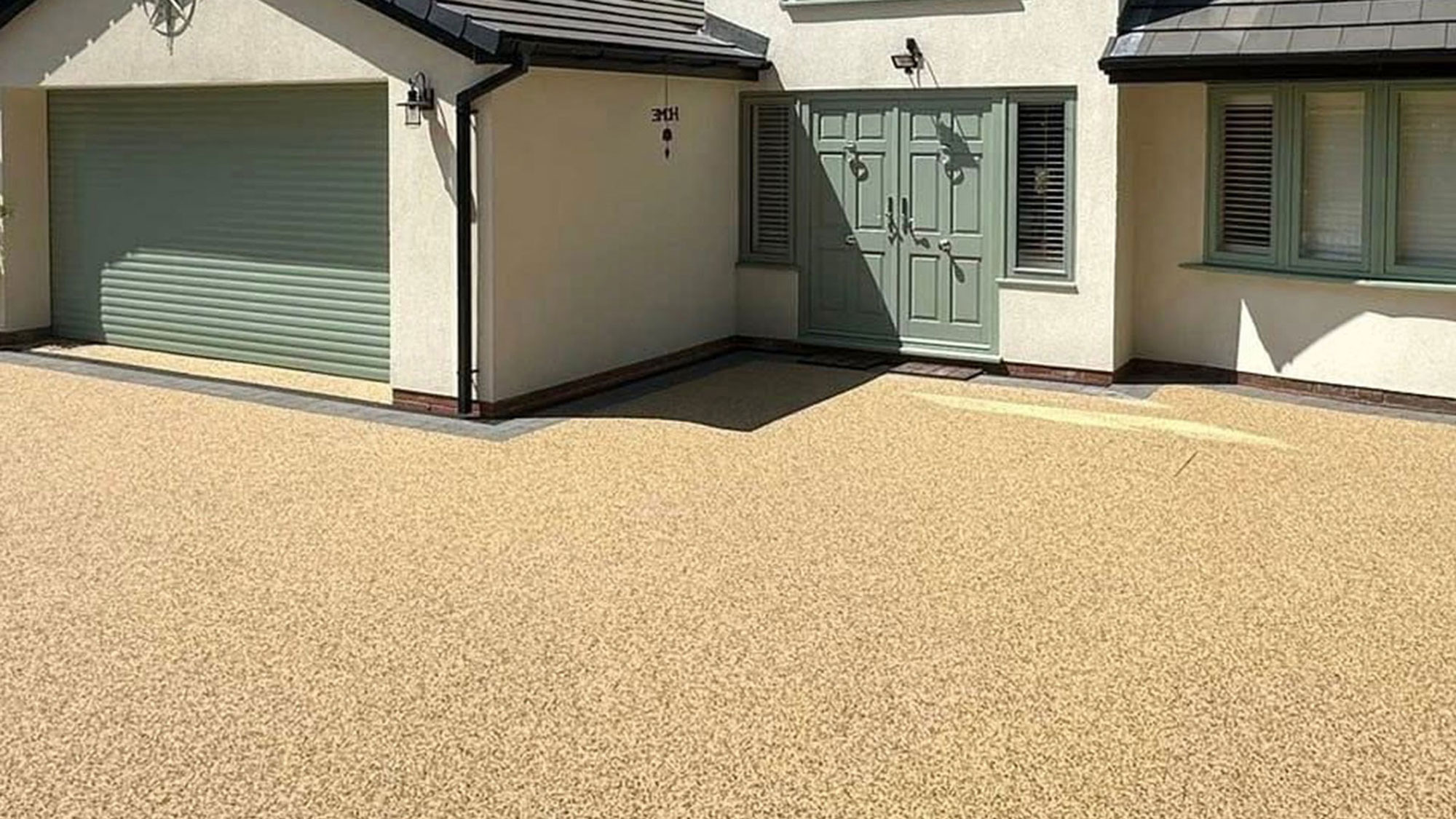 beige resin driveway in front of modern rendered house with sage green front and garage door