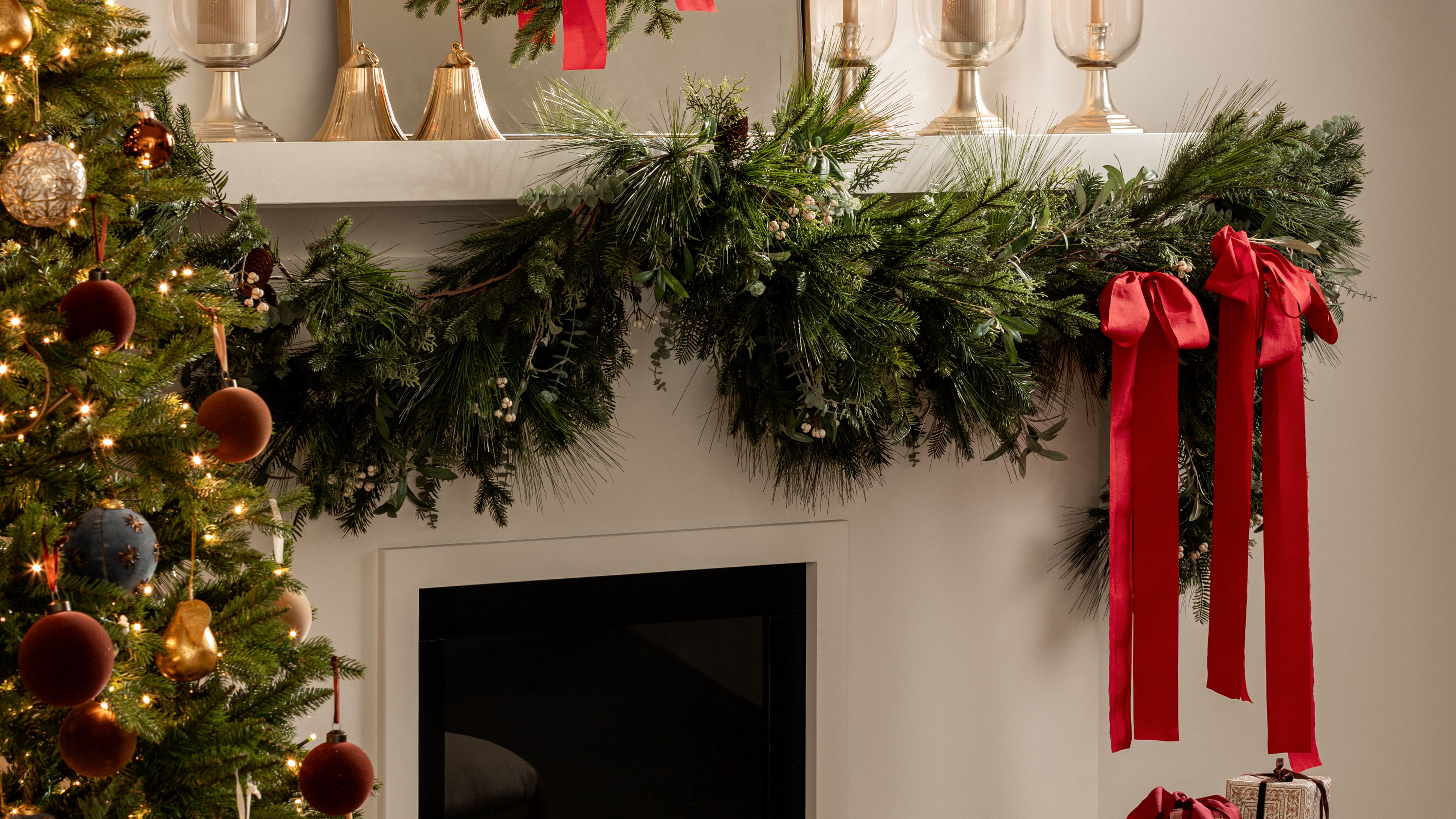 Festive holiday mantel styled with evergreen garland, brass bells, and red bows 