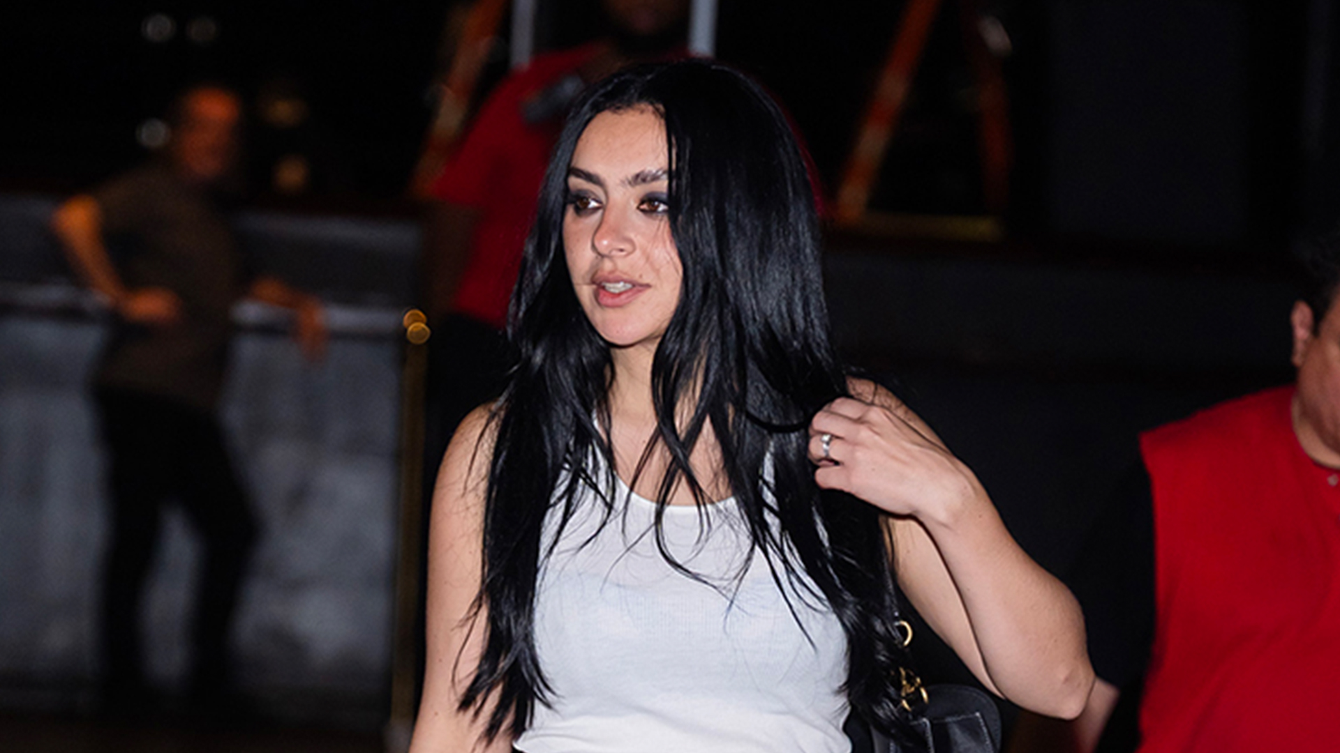 Charli XCX wearing a white tank top, black cropped pants, and black heels.