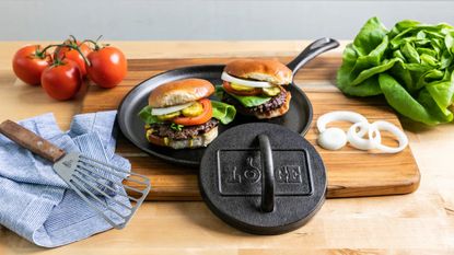 A Lodge cast iron burger press leaning against a plate of two burgers