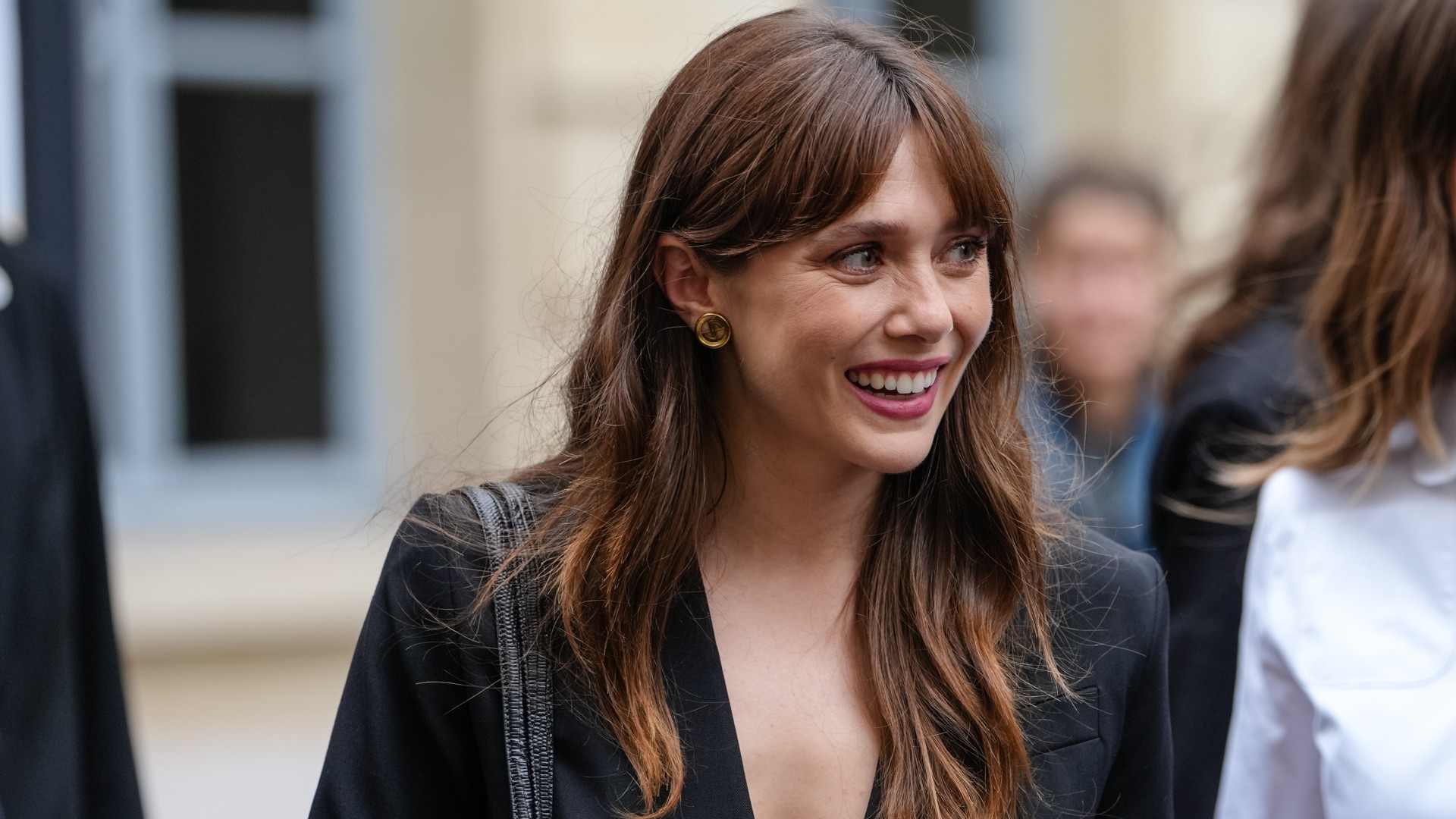 a white woman with dark hair and bangs being photographed by paparazzi