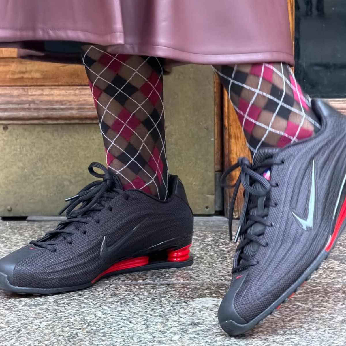 Tori Vanbreugel is photographed wearing Nike Shox Z trainers in black and red with a burgundy skirt and patterned tights.