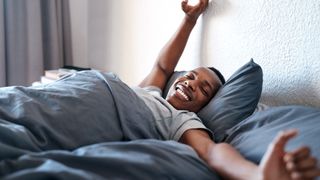 A man wakes up in bed and stretches after a good night's sleep