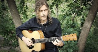 Mikael Åkerfeldt with his Martin OM Signature model, playing a few notes with trees in the background.