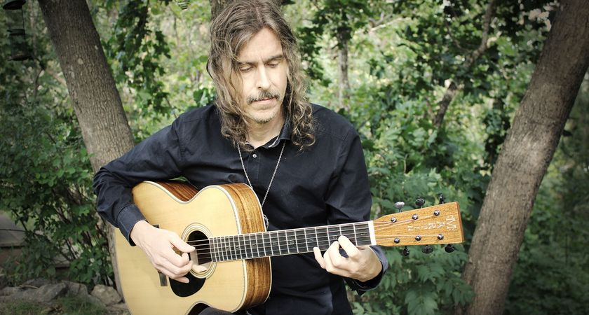 Mikael Åkerfeldt with his Martin OM Signature model, playing a few notes with trees in the background.
