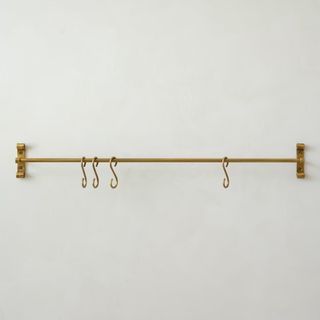 A brass toned rail with two wall brackets, four s hooks hanging from it