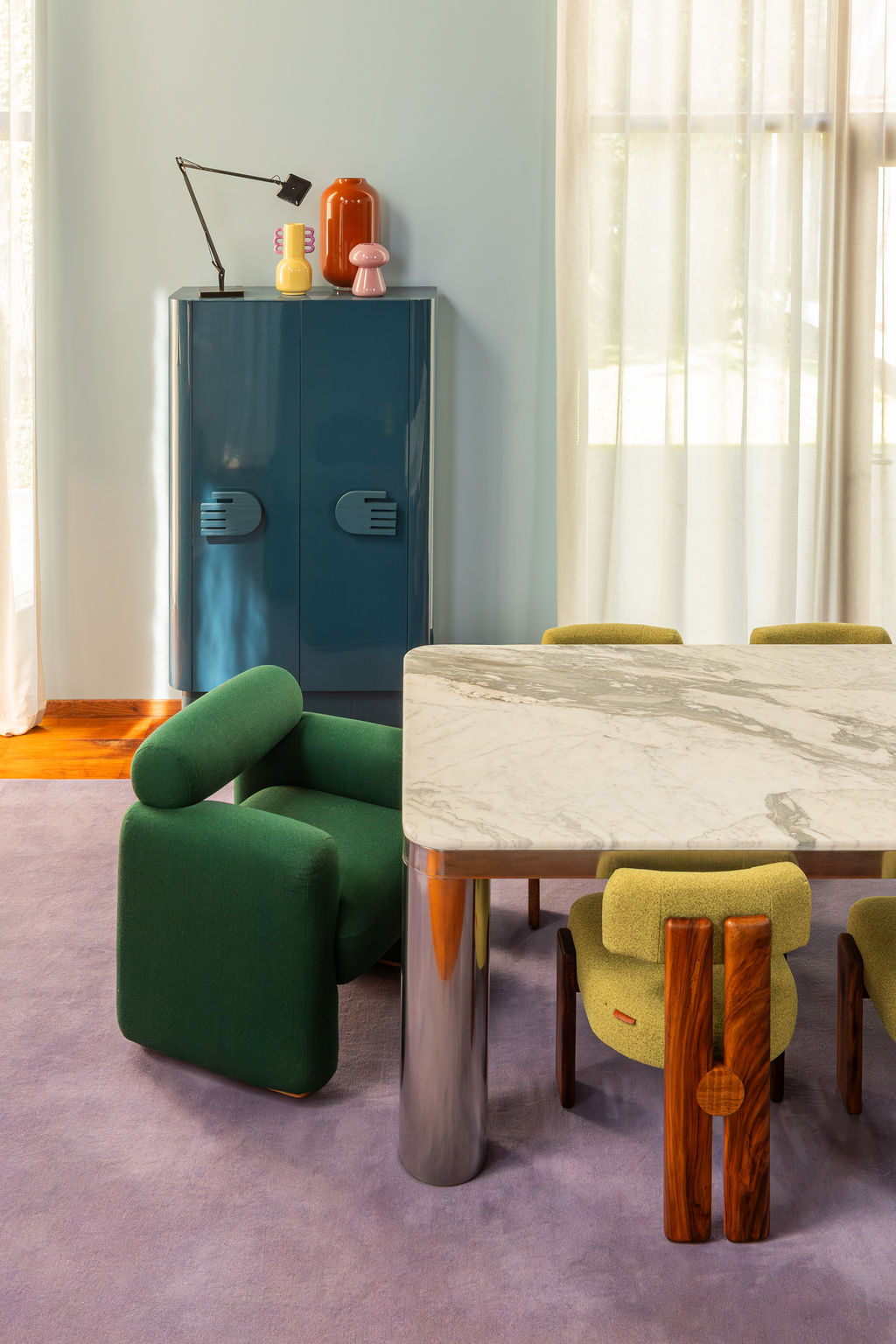 dining table with lilac rug, light blue walls, dark blue cabinet, sheer curtains, green armchair, and marble table with metal legs, and bright green-and-timber dining chairs