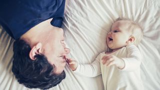 Mattress maker Tuft & Needle launches program for sleep-deprived new parents: A father lies on a mattress next to his laughing baby