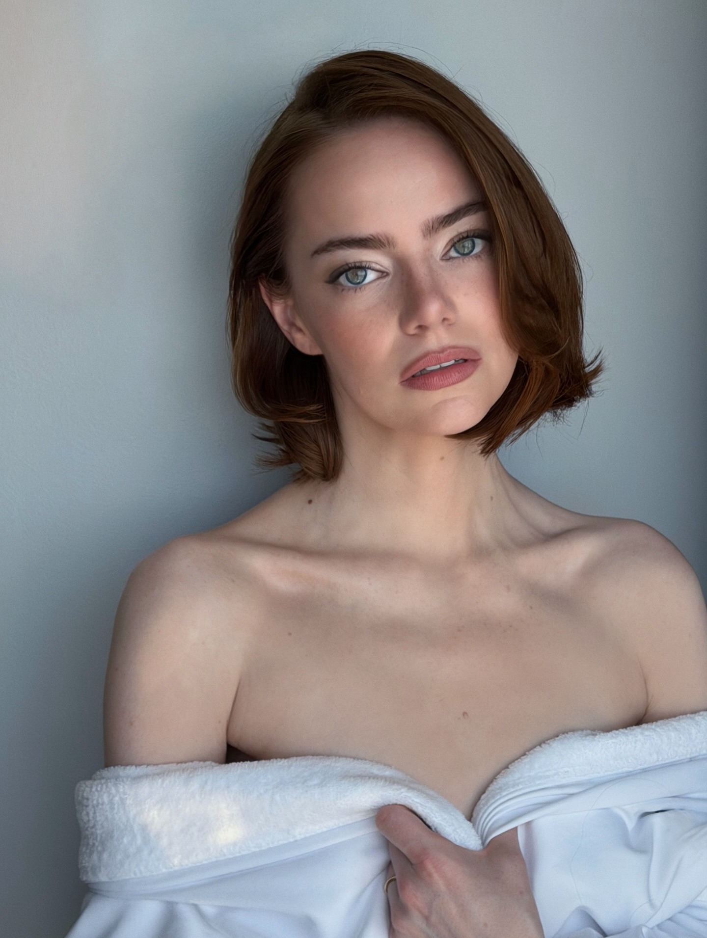 Emma Stone wearing a white robe with a full face of makeup and a short, flicky bob hairstyle