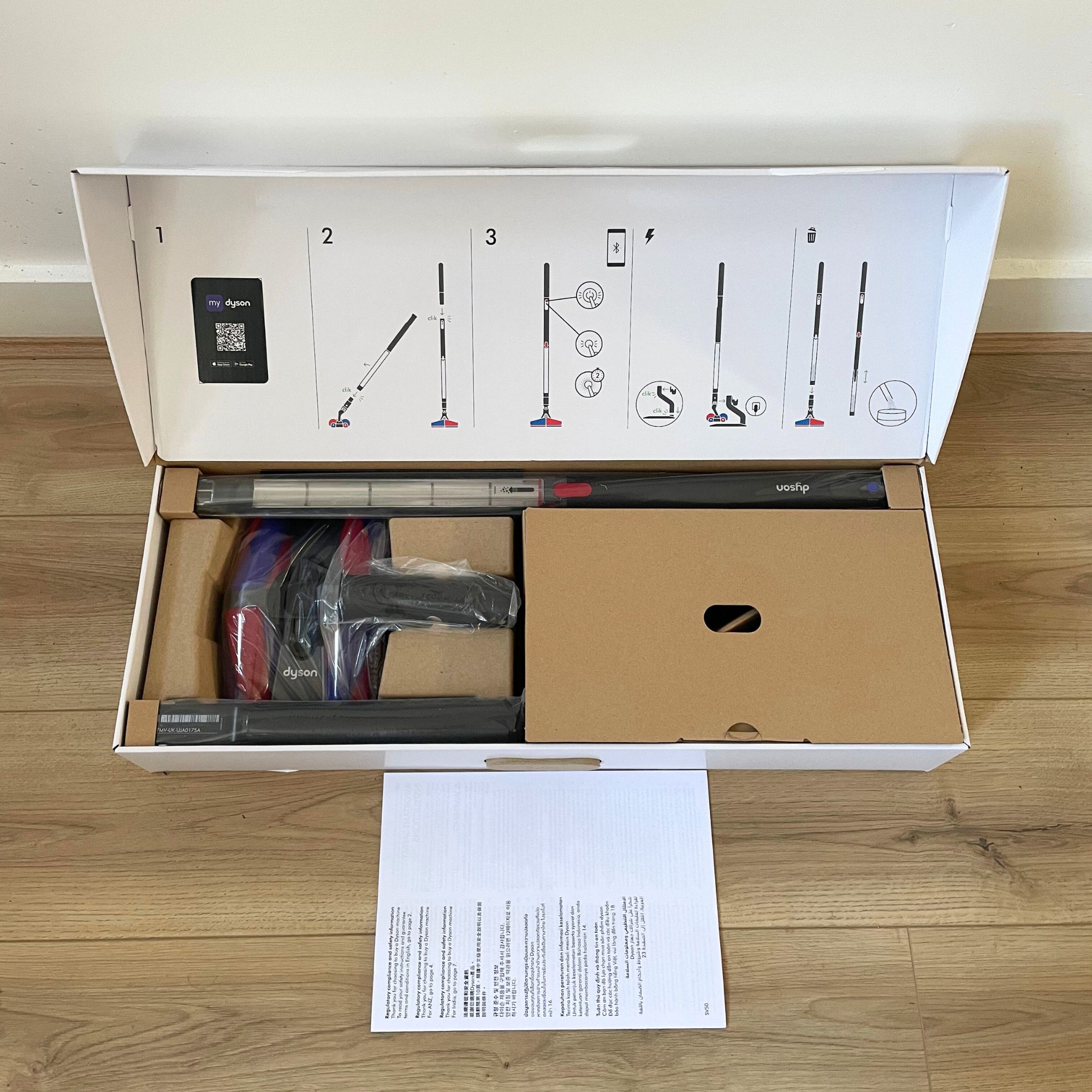 Dyson PencilVac box opened on wooden flooring, showing the components inside of it