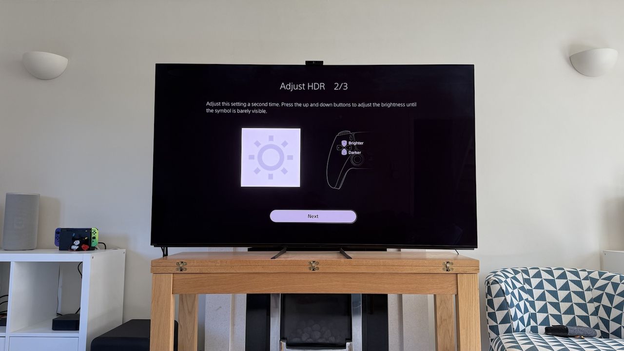 The 65-inch Sony A95L pictured on a wooden table in a living room. On the screen is the PS5 Adjust HDR menus