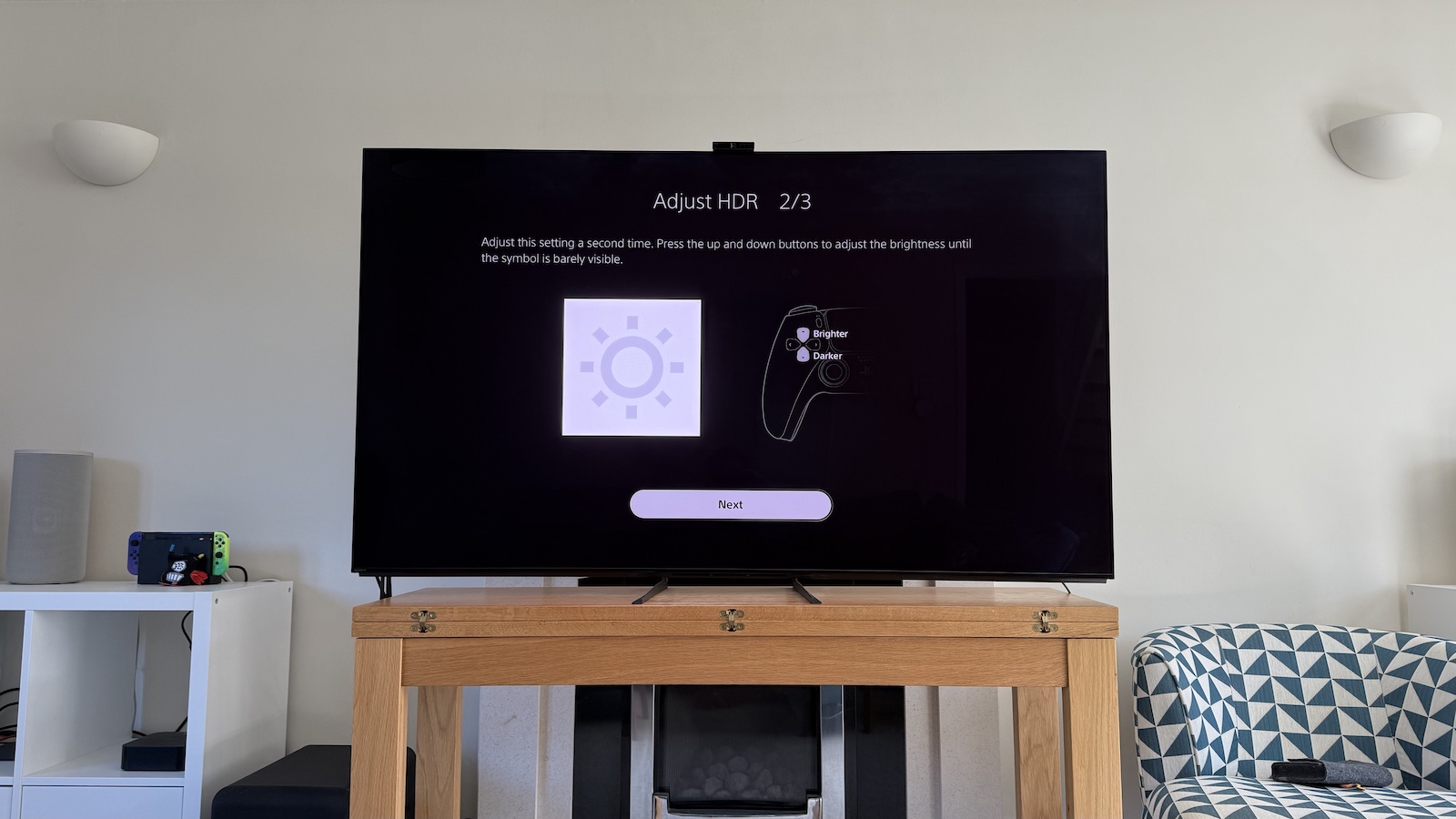 The 65-inch Sony A95L pictured on a wooden table in a living room. On the screen is the PS5 Adjust HDR menus