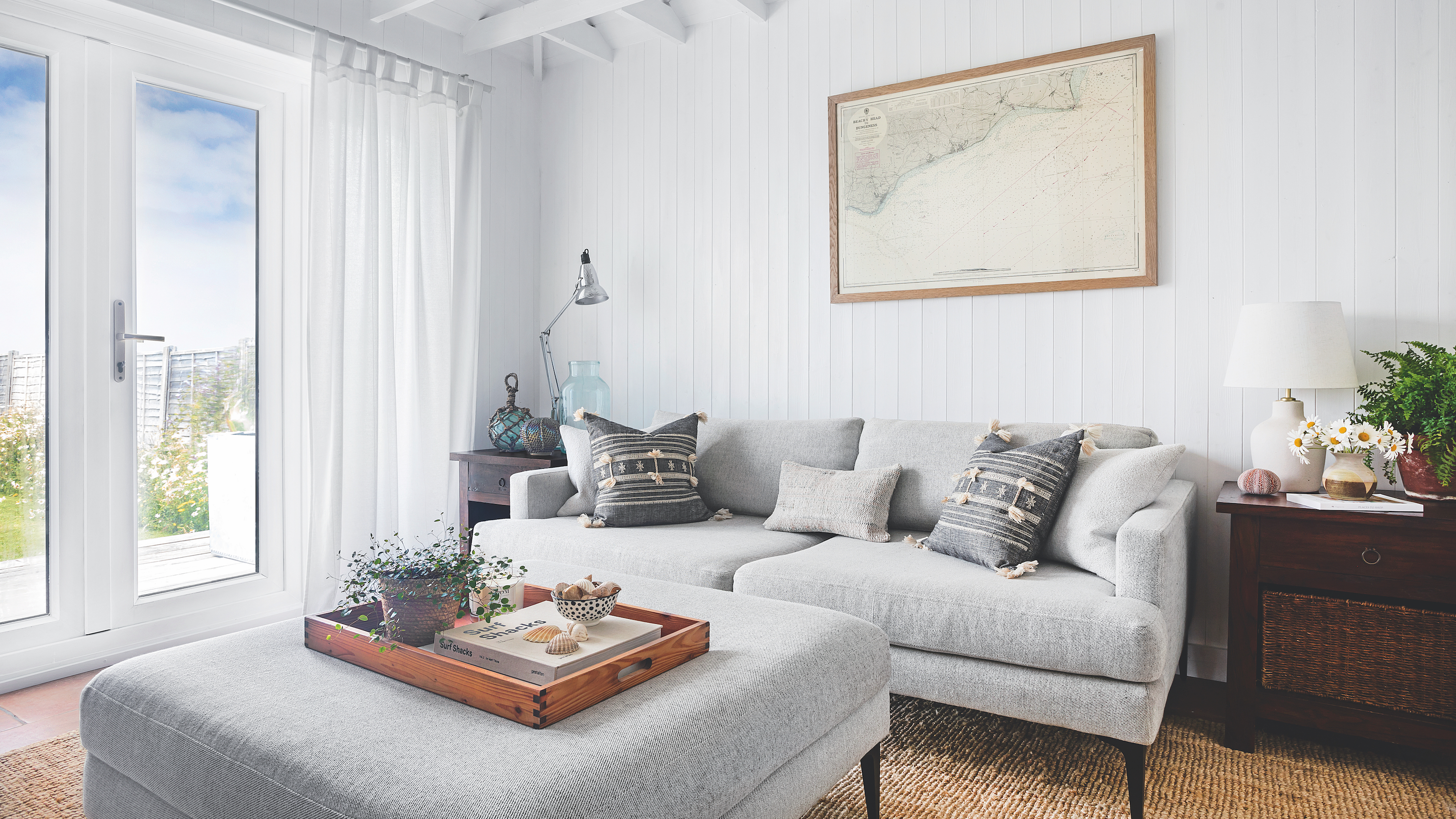 Coastal style sitting room with wood panelled walls and pale grey sofa with map print on wall
