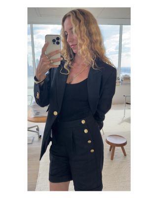 Woman wears navy blue oversize blazer and matching navy blue shorts with nautical, oversize buttons while talking mirror selfie.