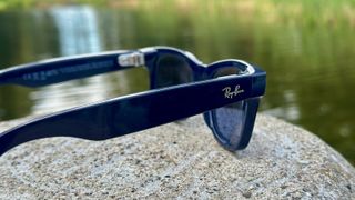 A photo of the Ray-Ban Meta (Gen 2) smart glasses sitting on a rock, angled to focus on the right arm with the Ray-Ban logo.