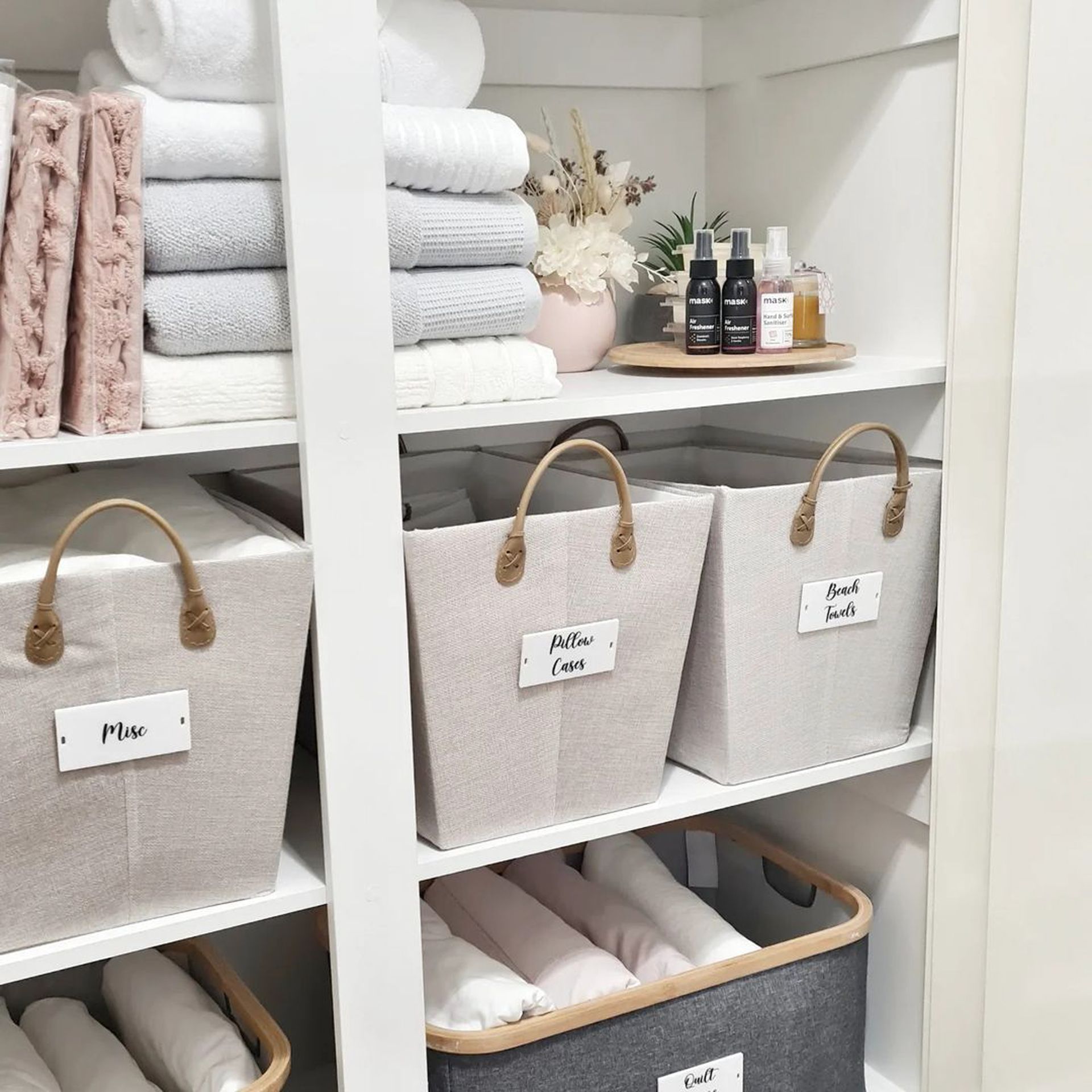 Lemari linen yang tertata dengan warna netral yang apik, dengan keranjang berlabel dari berbagai kategori linen.