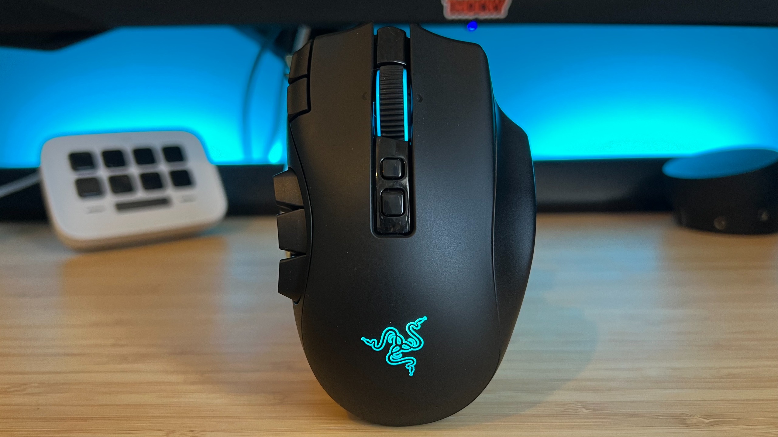Razer Naga V3 Pro gaming mouse standing upright on a wooden desk with blue backlighting