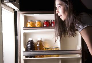 A woman looks in her fridge for a snack.
