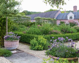 How to design a patio in a formal country cottage garden with gravel, stone patio and large planter pots.