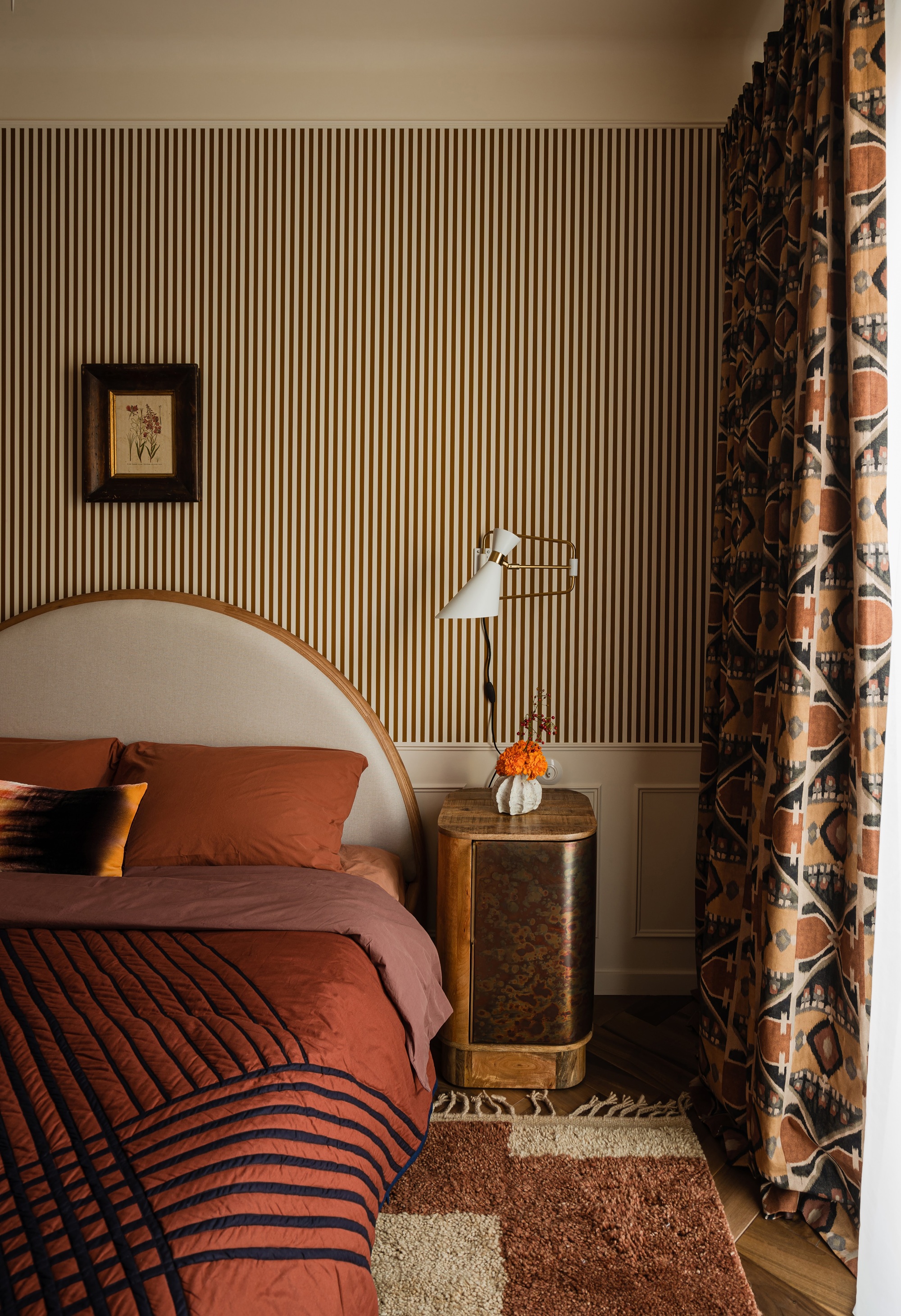 a bedroom with striped wallpaper, a semi circle bedhead, and burl sideboard furniture
