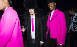 Four male models wearing looks from Dsquared2's collection. Two models are wearing white shirts and bright pink jackets. Another model is wearing a white shirt, pink tie, jeans, black coat and oversized fur hat. And the last model is wearing black trousers, a white shirt, bow tie and white waistcoat with black detail