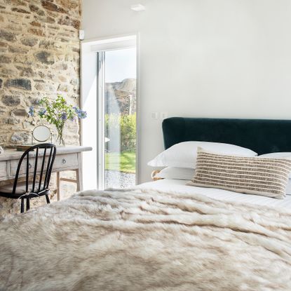 Bedroom with throw on bed, exposed brick wall and window into garden