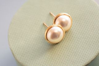 A close up of a pair of pearl earrings on a pale green background.