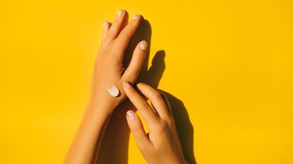 Woman spreading cream on hands with yellow background