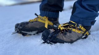 A pair of feet wearing Scarpa Mescalito TRK Pro GTX hiking boots in the snow, with crampons attached