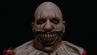 Close-up of Twisty The Clown without hat standing outside carnival entrance in American Horror Story: Freak Show
