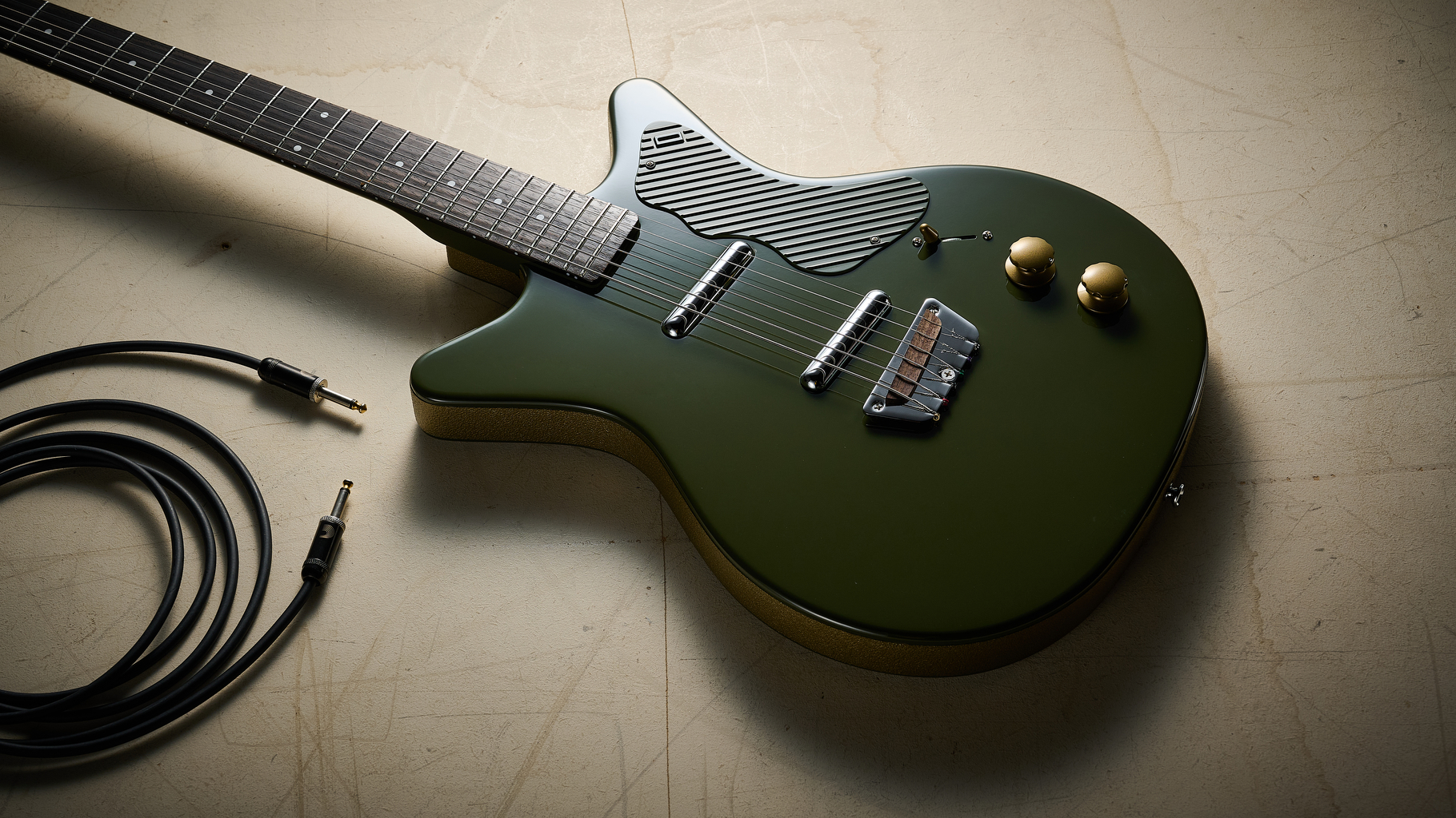 A Danelectro Dan O Cool Baritone guitar on an off white floor with a guitar cable nearby